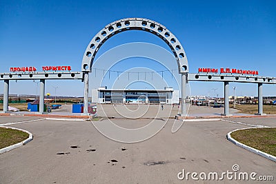 Celebration Square named after V.P. Mazikina with a large arch at the entrance, and the ice palace of sport where people walk with Editorial Stock Photo