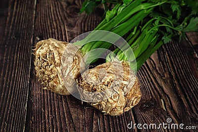 Celeriac roots with green leaves on dark wooden boards Stock Photo