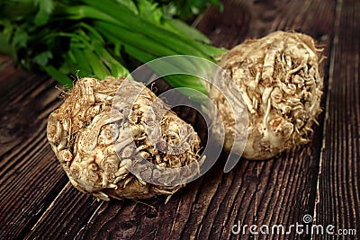 Celeriac / turnip-rooted celery roots with green leaves on dark wooden board, closeup detail Stock Photo