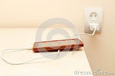 Cell phone is being charged from the electrical outlet Stock Photo