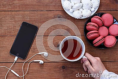 Cell phone with headphones, meringue, macaroons and a Cup of tea on wooden background Stock Photo