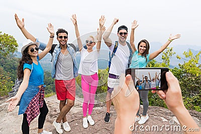Cell Smart Phone Taking Photo Of Cheerful Tourist Group With Backpack Over Landscape From Mountain Top, People Posing Stock Photo
