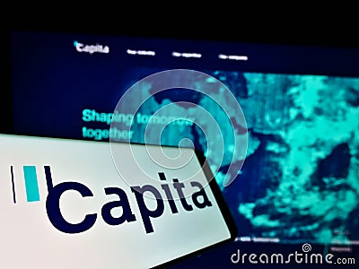 Cellphone with logo of British process outsourcing company Capita plc on screen in front of website with map. Editorial Stock Photo