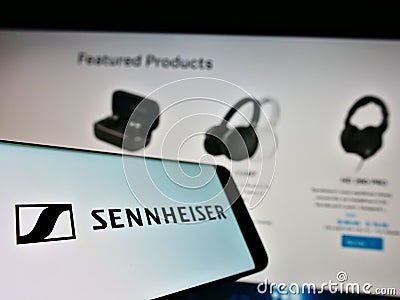 Cellphone with logo of German audio company Sennheiser electronic GmbH Co. KG on screen in front of web page. Editorial Stock Photo