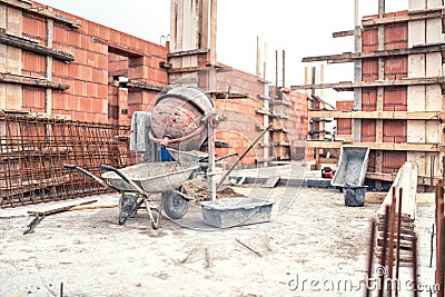 Cement mixer machine at construction site, tools, wheelbarrow, sand and bricks at house building. Stock Photo