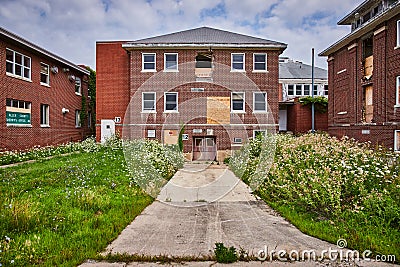 Cement path leading to entrance of large abandoned brick hospital buildings Stock Photo