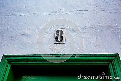 Ceramic black number 8 white wall over green door Stock Photo