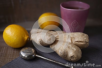 Ceramic mug of hot tea with tea strainer, ginger root and lemons on the table. Organic Alternative Therapy Concept. Stock Photo