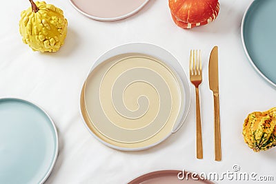 Ceramic plates with fork and knife and pumpkins serving background on white tablecloth. Top view, mockup Stock Photo