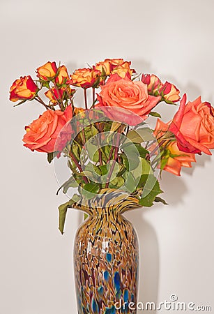 Ceramic vase, filled with four long stemmed, orange roses and a dozen baby, orange and red roses Stock Photo
