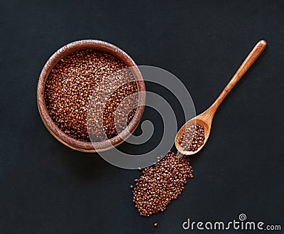 The cereal Buckwheat in wooden bowl with wooden spoon on black background, top view Stock Photo