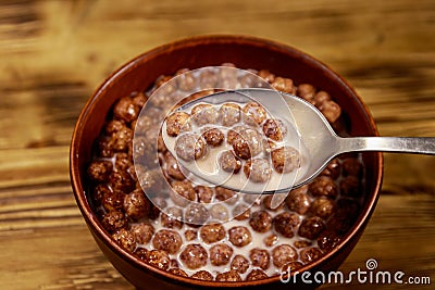 Cereal chocolate balls with milk in a bowl on wooden table. Spoon with breakfast Stock Photo