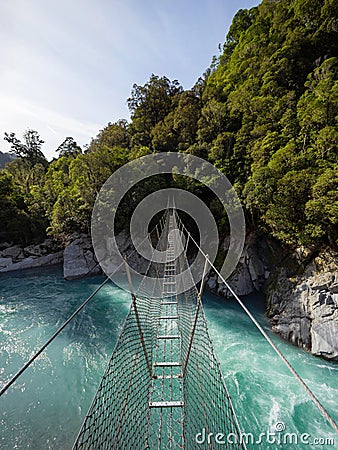 Cesspool Gorge hanging swing bridge leading over turquoise crystal clear blue Arahura River, West Coast, New Zealand Stock Photo