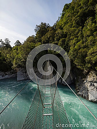 Cesspool Gorge hanging swing bridge leading over turquoise crystal clear blue Arahura River, West Coast, New Zealand Stock Photo