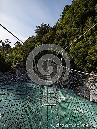 Cesspool Gorge hanging swing bridge leading over turquoise crystal clear blue Arahura River, West Coast, New Zealand Stock Photo