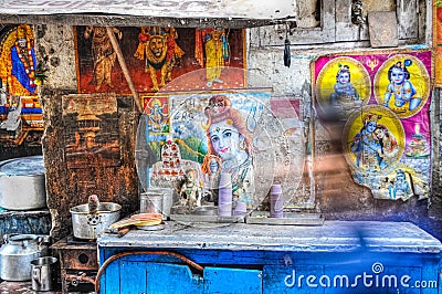 Chai tea street food stall with posters of shiva the god on the wall and a blurry person walking by in Delhi India Editorial Stock Photo