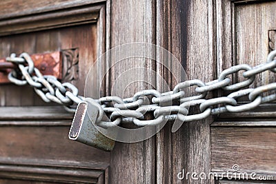 A chain of silver color with closed padlock on an old gate. Closeup of old wooden door with closed padlock on a chain. Stock Photo