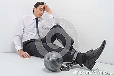 Chained businessman. Full length of depressed businessman sitting on the floor with shackles chained to his legs Stock Photo