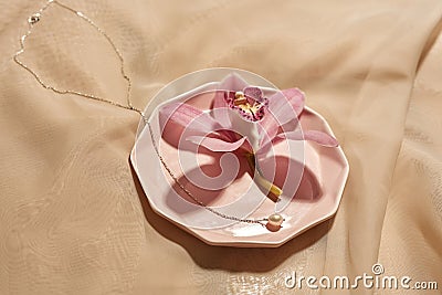 Chainlet and pink flower on plate on silk cloth Stock Photo