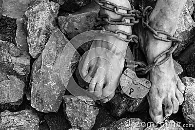 Chains with a lock on the legs of a slave amidst stones. Chains at the ankle. The symbol of slavery Stock Photo