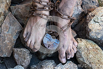 Chains with a lock on the legs of a slave amidst stones. Chains at the ankle. The symbol of slavery Stock Photo