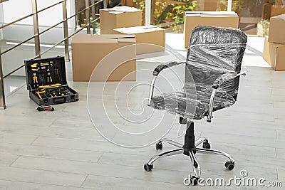 Chair wrapped in film and packed belongings in office. Moving service Stock Photo