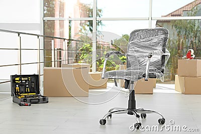 Chair wrapped in film and packed belongings, space for text. Moving service Stock Photo
