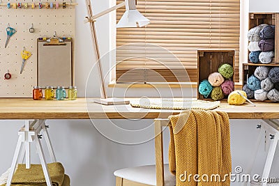 Chair with yellow blanket at desk with lamp and colorful yarns in workspace interior. Real photo Stock Photo