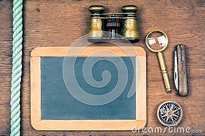 Chalk board, binoculars, compass, magnifying glass, knife, rope on wooden background Stock Photo