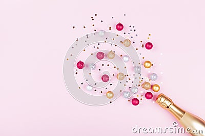 Champagne bottle with confetti stars and holiday balls on pastel pink background. Christmas pattern. Flat lay style Stock Photo