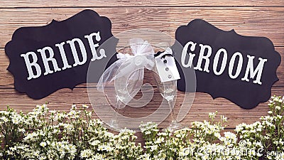 Champagne glass in wedding dress with Bride and Groom text sign on wooden background decorated with tiny white flower, vintage Stock Photo