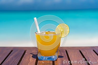 Champagne Mango-lime aqua fresca cocktail with straw on wooden table ocean background at the beach Stock Photo