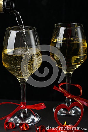 Champagne is poured into glasses tied with a ribbon on a black background next to a heart a candlestick with a burning candle Stock Photo