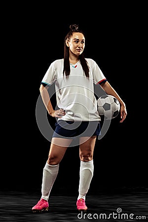 Full-length portrait of sportive girl, female soccer, football player posing isolated on black studio background. Sport Stock Photo