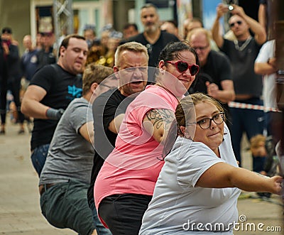 Championship in bus pulling on a thick rope with a team of three men and two young strong women with glasses Editorial Stock Photo