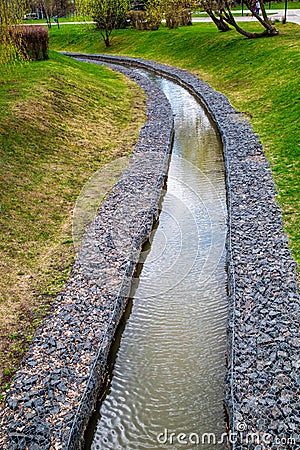 A channel made of granite stones for a stream of a river with green grass on the banks in a city park. Landscaping Stock Photo