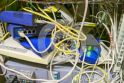 Chaotic interlacing of wires between modems, switches and Internet bridges. Rack with many network devices and cables. Box with Stock Photo