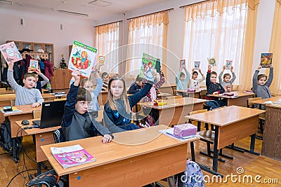 Schoolboys and schoolgirls sitting at their desks show textbooks to teacher holding them over their heads Editorial Stock Photo