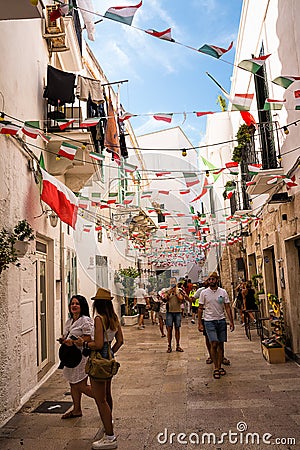 Characteristic alley with flags hanging and people tourists in the center of Monopoli Puglia Editorial Stock Photo