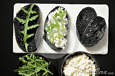 Charcoal black rye bread with cottage cheese and rocket on a black background Stock Photo