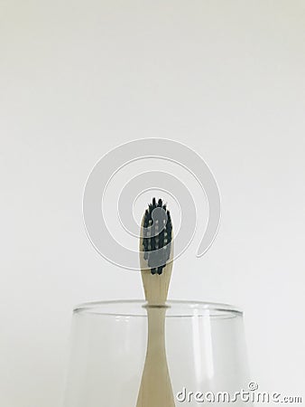 Charcoal infused bamboo toothbrush in glass with off white background Stock Photo