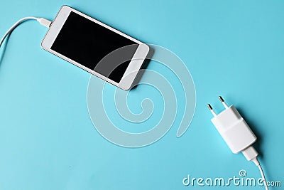 Close up white Smartphone Plug In with Charger Adapter on Blue Background Stock Photo