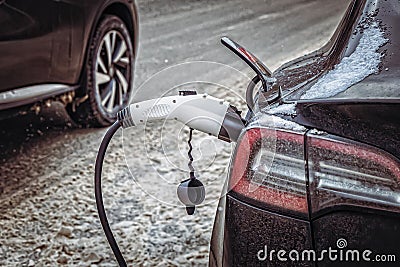 Charging the electric car in winter. Close-up of the charging cable plug inserted into the charging port of the electric Stock Photo