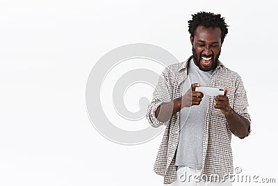 Charismatic, carefree african-american bearded man playing awesome smartphone game, holding mobile phone horizontally Stock Photo