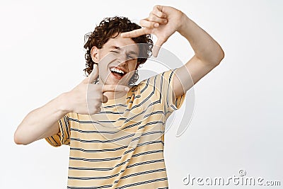 Charismatic curly guy looking through hand frame and laughing, imaging smth, searching angle point of view, standing Stock Photo