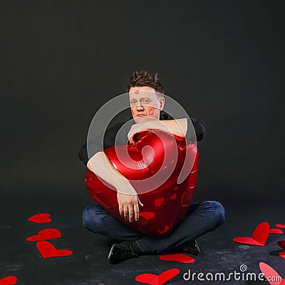 Charismatic guy holds a heart balloon inflatable in lipstick face Valentine symbol, flirting, on the floor hearts Stock Photo