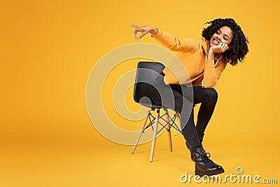 Charming african american young woman with beautiful smile dressed in casual clothes sitting on the stylish chair and Stock Photo