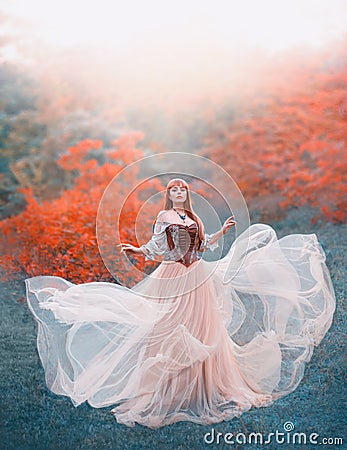 Charming attractive girl with long flying waving peach light vintage dress stands alone in forest, innocent lady looks Stock Photo