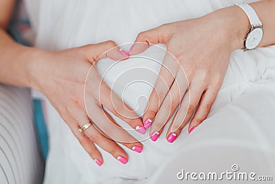 Charming tummy which the pregnant woman in a white dress embraces. The pregnant girl with pink manicure embracing belly Stock Photo