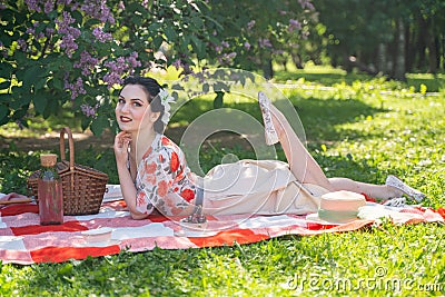 A charming brunette young girl enjoys a rest and a picnic on the green summer grass alone. pretty woman have a holiday and spend v Stock Photo